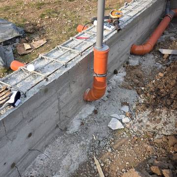 Bajante de saneamiento con codo y abrazadera junto a un muro